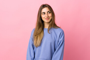 Young woman over isolated pink background having doubts while looking side