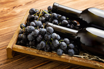 Two Red Wine bottles composition on brown wooden table. Red wine bottles in box on black ripe...