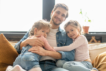 Portrait of handsome father and his cute daughters hugging and smiling.