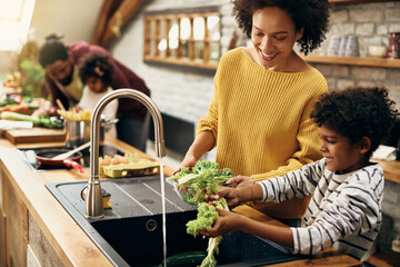 Happy black mother and son watching salad while preparing food in the kitchen.