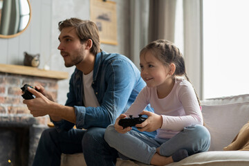 family, gaming and entertainment concept - happy father and little daughter with gamepads playing video game at home. © opolja