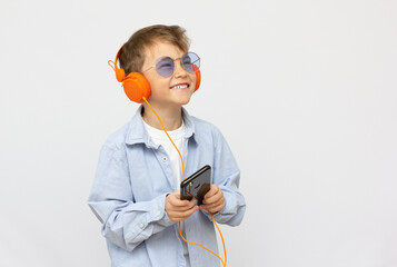 Smiling boy in sunglasses listening to music on headphones with phone