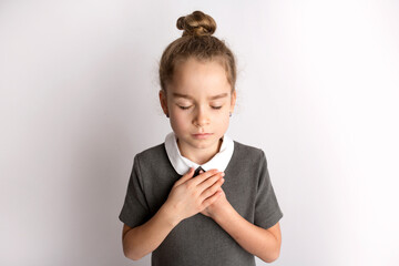 Attractive little girl in a strict school dress, stands on a white background with empty copy space, gestures with her hands, admires a happy expression on her face