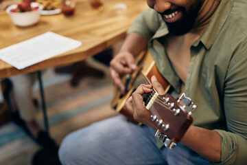 Close-up of black man playing acoustic guitar at home.