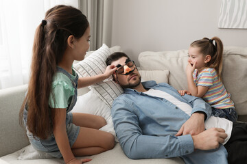 Cute little children putting funny glasses on father while he sleeping at home