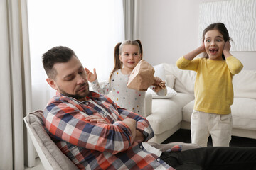 Cute little children popping paper near father while he sleeping at home