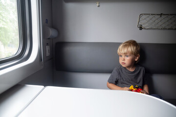 Kid in a train compartment looks out the window. The passenger travels in the train cabin