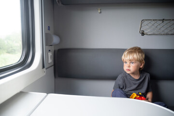 Kid in a train compartment looks out the window. The passenger travels in the train cabin and holds a toy