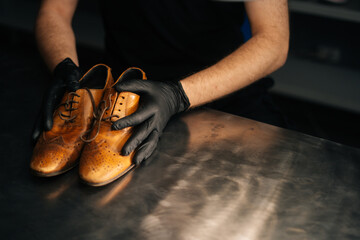 Close-up top view of hands of shoemaker shoemaker in black gloves holding old worn light brown...