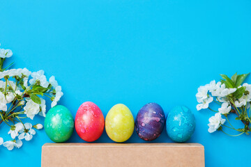 Five colorful easter eggs and flowers on blue background.