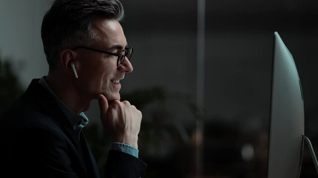 A side view of a happy businessman is using his wireless earphones sitting in the office in the evening
