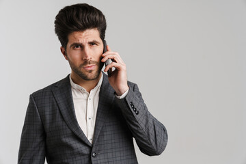 Serious young man in jacket posing and talking on mobile phone
