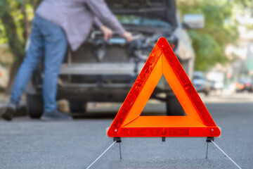 Red emergency stop triangle sign afore Destroyed car in car crash traffic accident on city road. Man driver looking on Smashed broken car in accident. Copy space