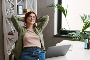 Young pleased woman with red hair resting while working with laptop