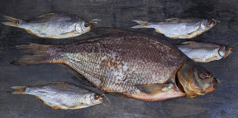 Salted and dried bream among several roach on black surface