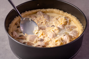 On the kitchen table is a mold of shortcrust pastry. Inside a mixture of mushrooms, chicken pieces, cheese and cream