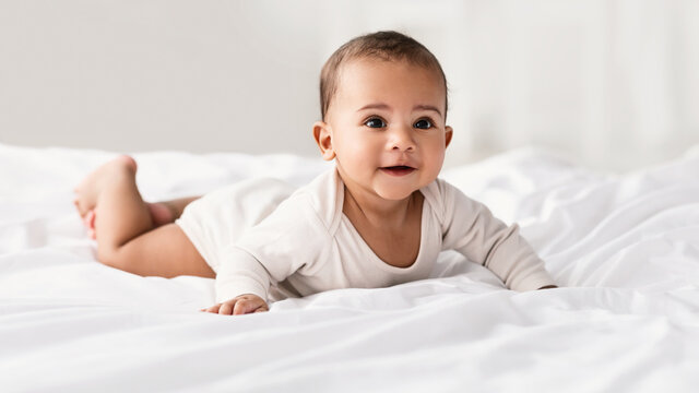 Cute little African American baby lying on bed at home