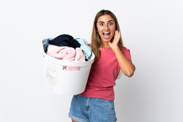 Young woman holding a clothes basket isolated on white background with surprise and shocked facial...