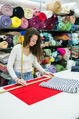 Side view of  brunette woman measuring fabric on work table in textile store. Seller working with tissue in drapery shop. Small Business Concept