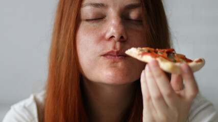 Young  chubby woman with long hair holding tasty big slice of pizza ready to eat at home