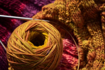 Wollknäuel in Ocker und Gelb auf Strickstück in rosa und Lila mit Stricknadeln 