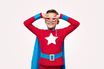 Excited preteen boy in superhero costume doing owl gesture in studio