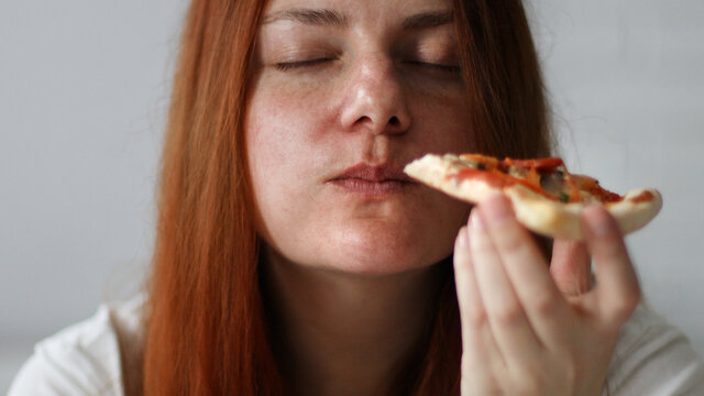 Young  chubby woman with long hair holding tasty big slice of pizza ready to eat at home