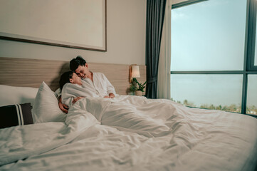 Obraz na płótnie Canvas Asian couple is hugging and smiling sitting on the bed in a bedroom evening.Couple in Valentine day.Love couple,Relationship and couple concept.