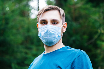 Caucasian man in medical face mask outside. Guy portrait in protective mask in park alone....