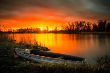 a small boat on the banks of a quiet river during sunset over the trees 