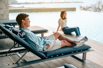 Asian couple sitting near pool with perfect sea view.Summer,Vacation,Love couple and sweet  couple concept.