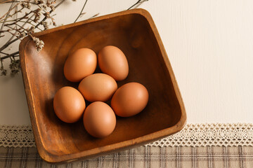 Easter eggs of natural color in a wooden plate on a checkered tablecloth on a light background.