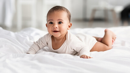 Cute little African American infant lying on white bed