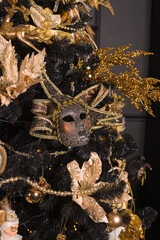 Christmas gold decorations on a black Christmas tree carnival mask, gold balls, beads. Close-up.
