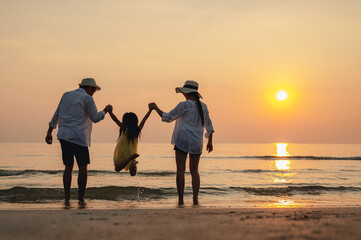 Happy asian family jumping together on the beach in holiday. Silhouette of the family holding hands enjoying the sunset on the  beach.Happy family and vacations concept.