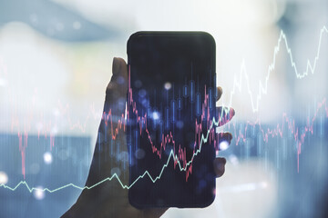 Double exposure of abstract creative financial chart and hand with cell phone on background,...