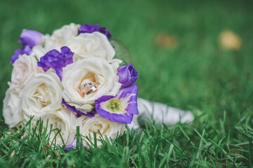 A bouquet of flowers lies on the green grass. The bride's bouquet. Wedding flowers. There are two wedding rings on the bouquet. Selective defocusing