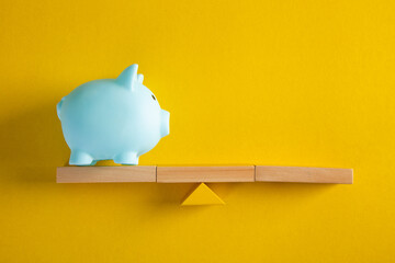 Piggy bank balancing on seesaw on yellow background