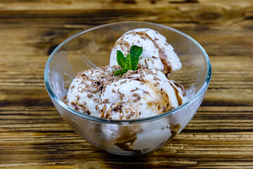 Glass bowl with ice cream balls, mint leaf and chocolate topping on a wooden table