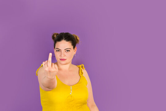 Mujer joven con la mano levantada mostrando un solo dedo medio levantado en gesto grosero sobre un fondo morado liso y aislado. Vista de frente. Copy space