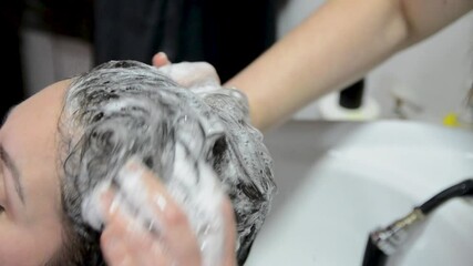 Young woman having hair washing in professional hairdressing salon. Hands of female hairdresser washes hair with foam and shampoo in beauty salon, close-up.   - Powered by Adobe