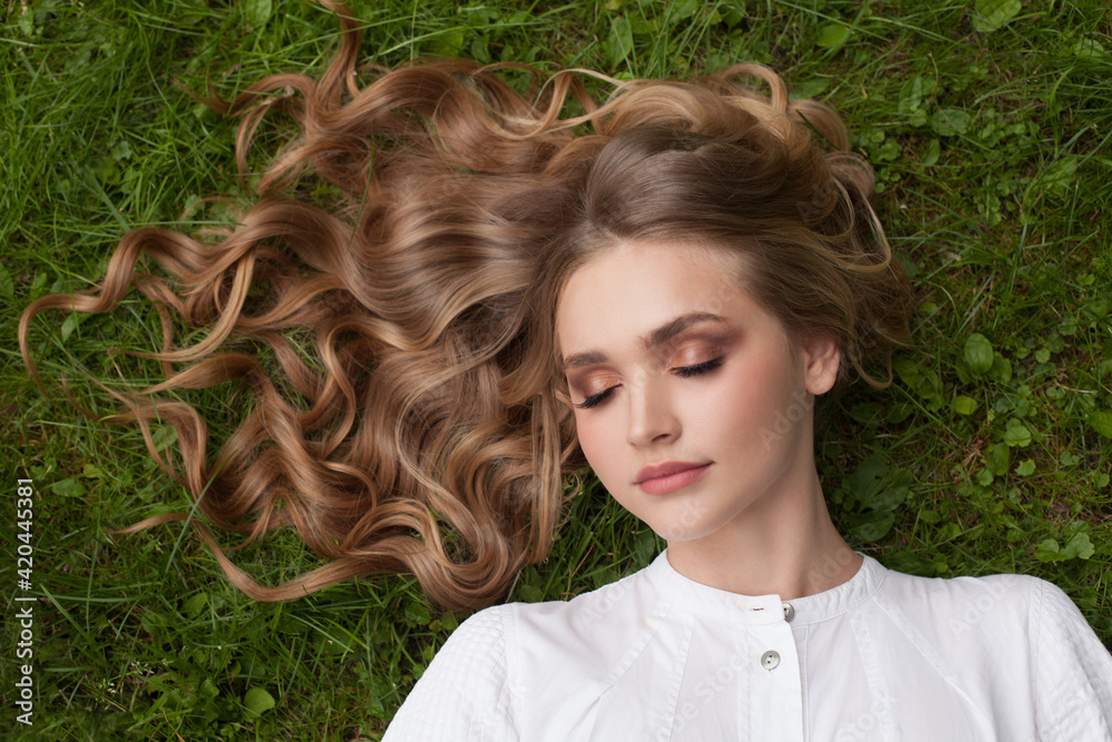 Wall mural carefree young woman with curly blonde hair lying on green grass outdoor