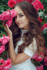 Beautiful portrait of a woman in poses. A brunette woman is standing next to roses in nature. High quality photo.
