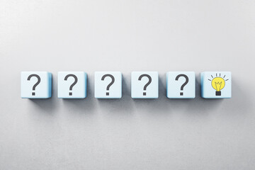 Idea and right solution concept with row of blue cubes with question mark and one with yellow light bulb on grey background