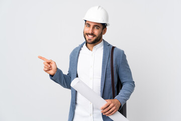 Young architect man with helmet and holding blueprints isolated on white background pointing finger to the side