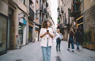 Trendy dressed travel blogger 20s exploring new city during getaway touristic vacations, Caucaisan hipster girl in stylish apparel using 4g wireless connecting on modern smartphone technology
