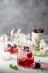 Cold cherry lemonade drink with fresh cherry and ice on gray background