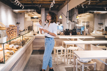 Professional Caucaisan sales representative working in small local bakery checking report for delivery order, self employed woman accounting in grocery service industry analyzing documents indoors