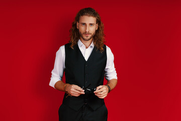 Charming young man in elegant clothing looking at camera while standing against red background