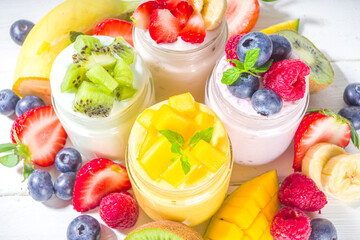 Set of various fruit and berry sweet yogurts in glass jars. Variety healthy Breakfast yoghurts with blueberry, strawberry, mango, kiwi, raspberry, with fresh fruits and berries